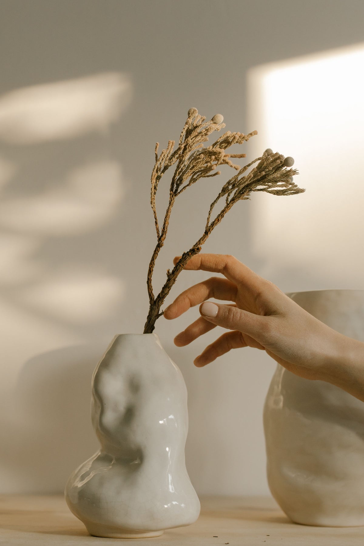 Hand placing a dried stem in a handmade white ceramic vase